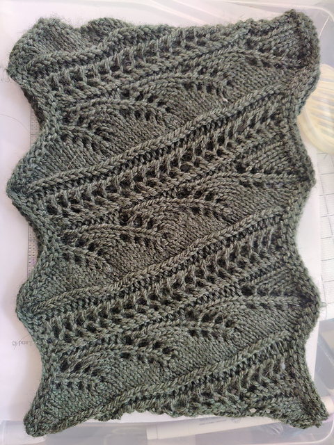 A cowl in green yard. It's lace and it looks like columns of wheat stalks. The edges are scalloped.