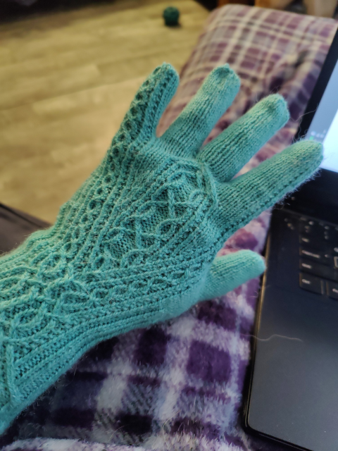 Gloves in a sort of pastel-ish green. Complex cabled pattern again. The cable pattern on the wrist splits around another cable pattern on the hand, and is reduced to two small chains going up the index and pinky fingers.
